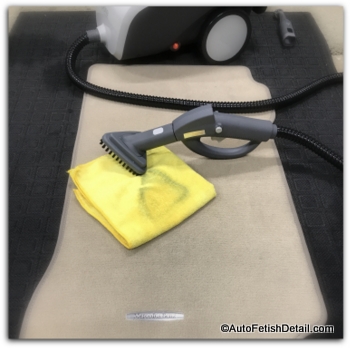 Pure steam cleaner sitting next to tan colored MBZ floor mat in the cleaning process of detailing a car Pure upholstery steam cleaner shampooing car floor mat
